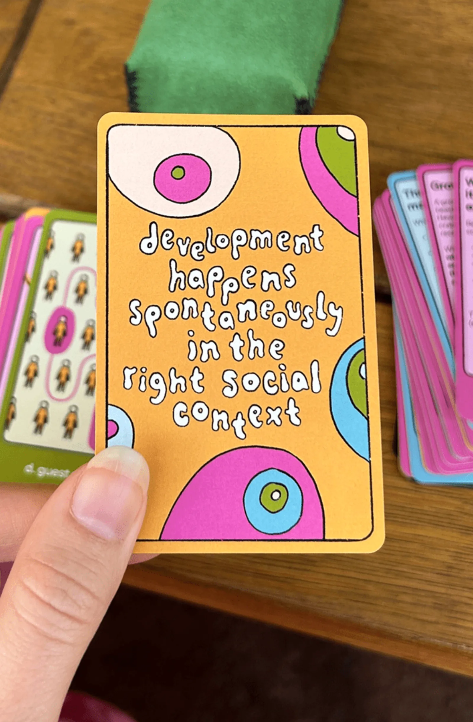 A hand holding an orange card reading: development happens spontaneously in the right social context