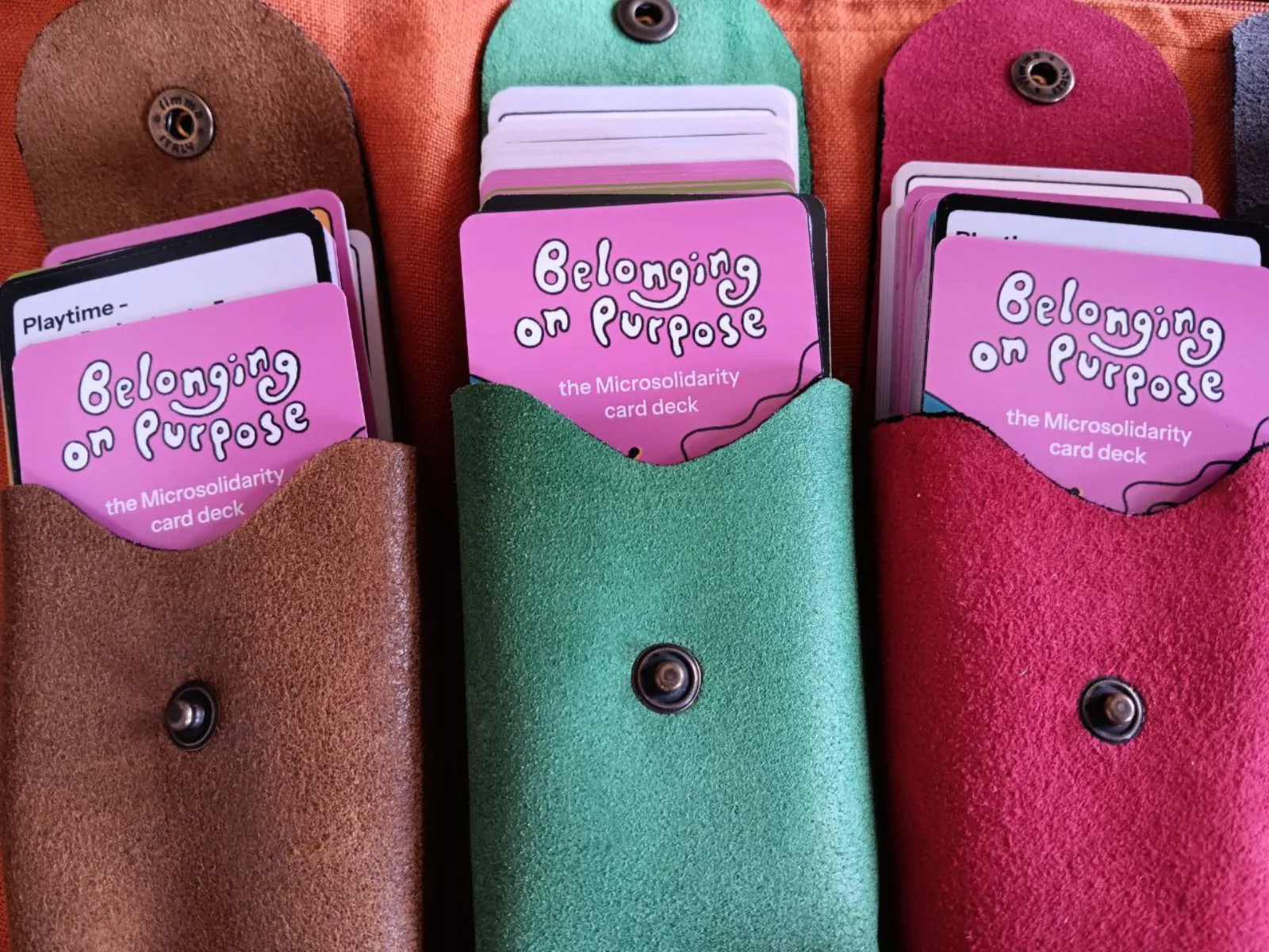 Three suede pouches holding copies of the Belonging on Purpose Microsolidarity card deck