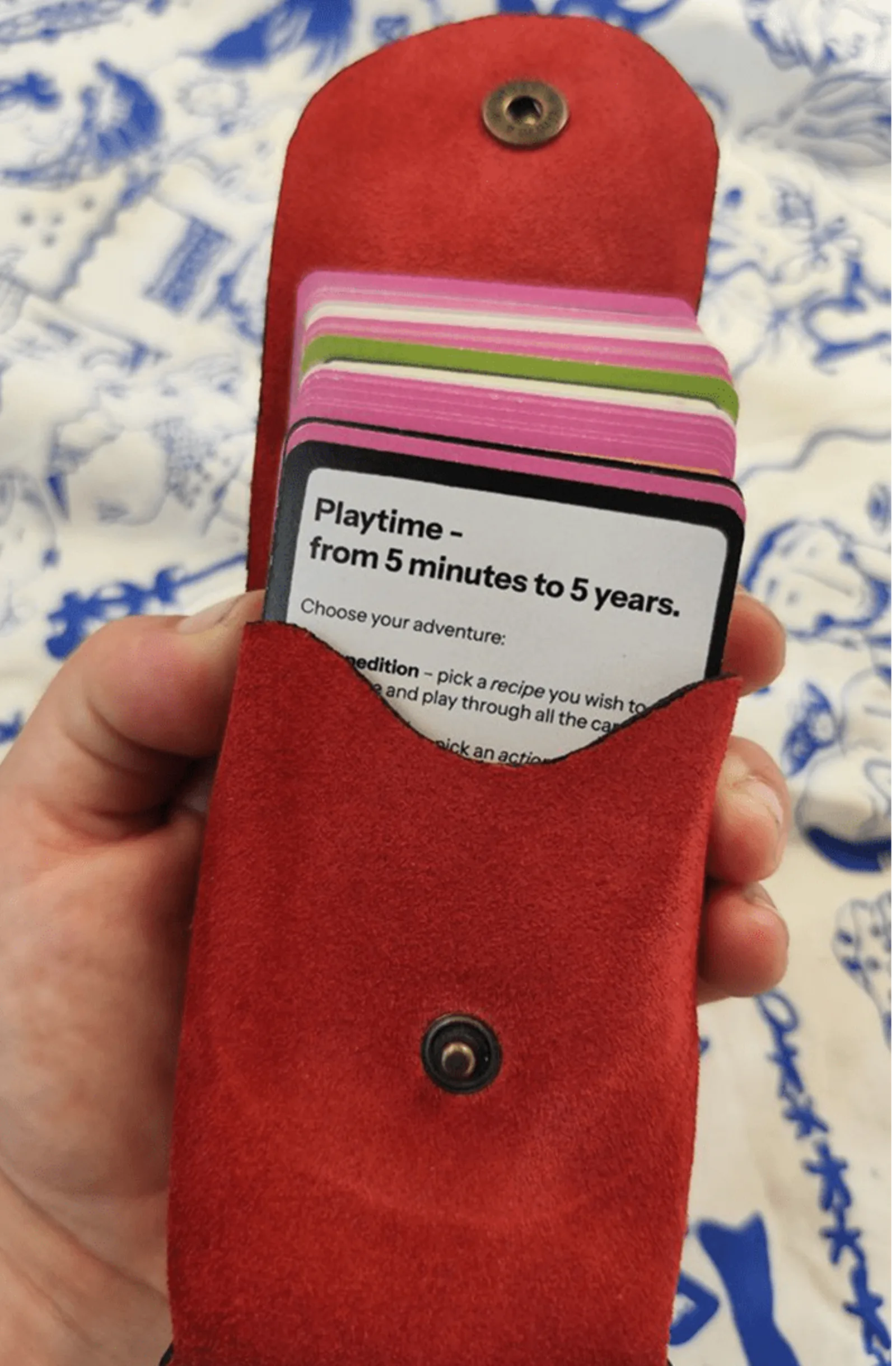 A hand holding a red suede pouch of cards, the top card reading: Playtime, from 5 minutes to 5 years